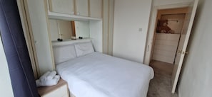 A bedroom with a bed, a bedside table with towels, a mirror, and a wardrobe.