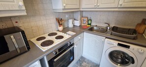 Una cocina compacta equipada con estufa, horno, microondas, lavaplatos y lavadora.