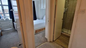 Una habitación de hotel con cama, mesita de noche, cómoda y zona de ducha.