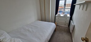 A small, narrow hotel room with a single bed, a bedside table, and a dresser with three drawers. - Waterfront 2BD Flat with Balcony, Central Dublin (Dublin)