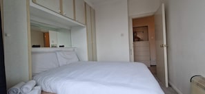 A neatly made bed with white linens and pillows, a large mirror above it, and a wardrobe with sliding doors.