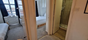 Habitación de hotel con cama, tocador, ducha y vistas a la ciudad desde la ventana.