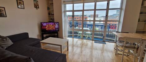 A living room with a sofa, a coffee table, a TV, and a view of the outside through large windows.