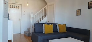 A living room with a dark-colored sofa, two yellow cushions, a white coffee table, and a staircase leading to another room. - Waterfront 2BD Flat with Balcony, Central Dublin (Dublin)