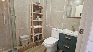 Une salle de bain comprenant des toilettes, un lavabo, un miroir, une étagère avec des articles de toilette et une poubelle.