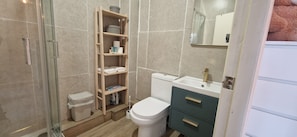 A bathroom with a toilet, a sink, a mirror, a shelf with toiletries, and a trash bin. - Waterfront 2BD Flat with Balcony, Central Dublin (Dublin)