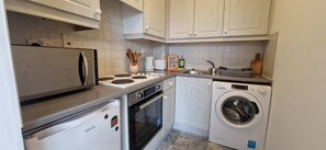 Une cuisine compacte équipée d’un réfrigérateur, d’une cuisinière, d’un four et d’un lave-linge.