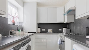 A compact kitchen with white cabinetry, a built-in washing machine, and a gray countertop. - Riverside 2BD Flat, Short Walk to the ExCel Centre (Greater London)