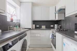 A compact kitchen with white cabinetry, a built-in washing machine, and a gray countertop. - Riverside 2BD Flat, Short Walk to the ExCel Centre (Greater London)