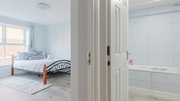 Een slaapkamer met een bed, een raam, een badkamer met een badkuip en een deur.