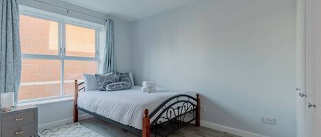 A bedroom with a bed, a nightstand, a window with curtains, and a view of a brick building.