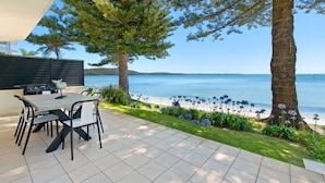 A patio with a dining table and chairs, overlooking a body of water with a boat in the distance.