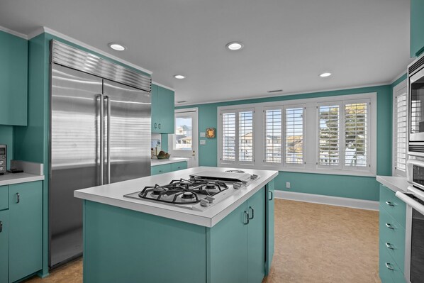 A kitchen with teal cabinetry, a stainless steel refrigerator, a gas stove, and a window with blinds.