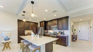 A modern kitchen with dark wood cabinets, stainless steel appliances, and a large island with bar stools. - Anglers Bay at One Particular Harbour 392-103 · Lagoon Views · 5-Night Min (Bradenton)