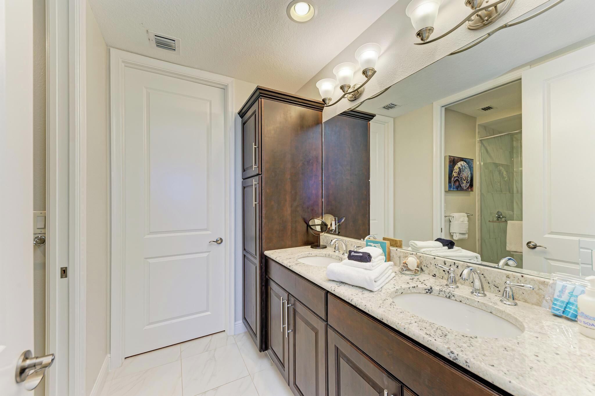 Une salle de bain dotée d’un meuble-lavabo à deux vasques, de meubles en bois foncé, d’un grand miroir et d’un luminaire fixé au plafond.