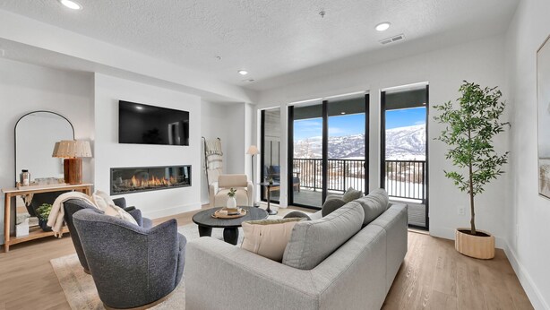 A modern living room with a fireplace, grey sofa, and a view of the mountains through large windows.