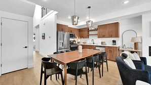 A modern kitchen with wooden cabinets, stainless steel appliances, and a dining area with a wooden table and black chairs.