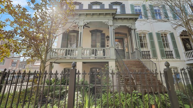A multi-story building with a balcony, a staircase, and a fenced garden area.