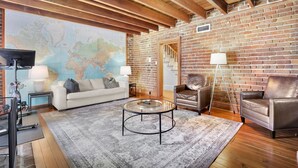 A spacious living room with a large world map on the wall, a leather sofa, a glass coffee table, and a wooden ceiling.