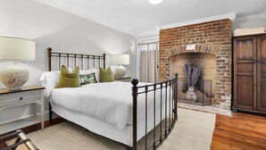 A bedroom with a bed, nightstands, a fireplace, and a wardrobe.
