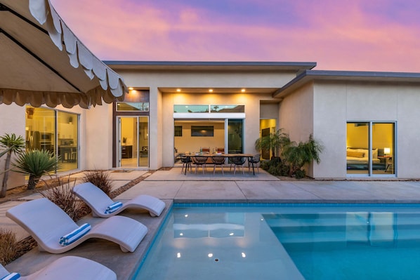 A modern house with a swimming pool, outdoor furniture, and a patio area.