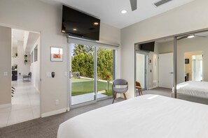 A modern hotel room with a large bed, a TV, a sliding glass door to a garden, and a small seating area.