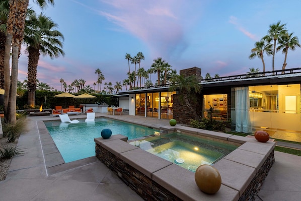 A pool area with lounge chairs, palm trees, and a modern building with large windows.