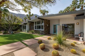 A modern house with a stone facade, large windows, and a well-maintained lawn with cacti. - The High Road – Iconic Mid-Century Retreat (Palm Springs)