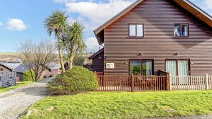 A two-story wooden cabin with a sloped roof, a front porch, and a gravel driveway. - The Palm Tree Lodge | Spacious contemporary 2 bed (Saint Columb Major)