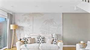 A modern living room with a white sofa, patterned cushions, a glass vase, and a wooden coffee table. - The Palm Tree Lodge | Spacious contemporary 2 bed (Saint Columb Major)