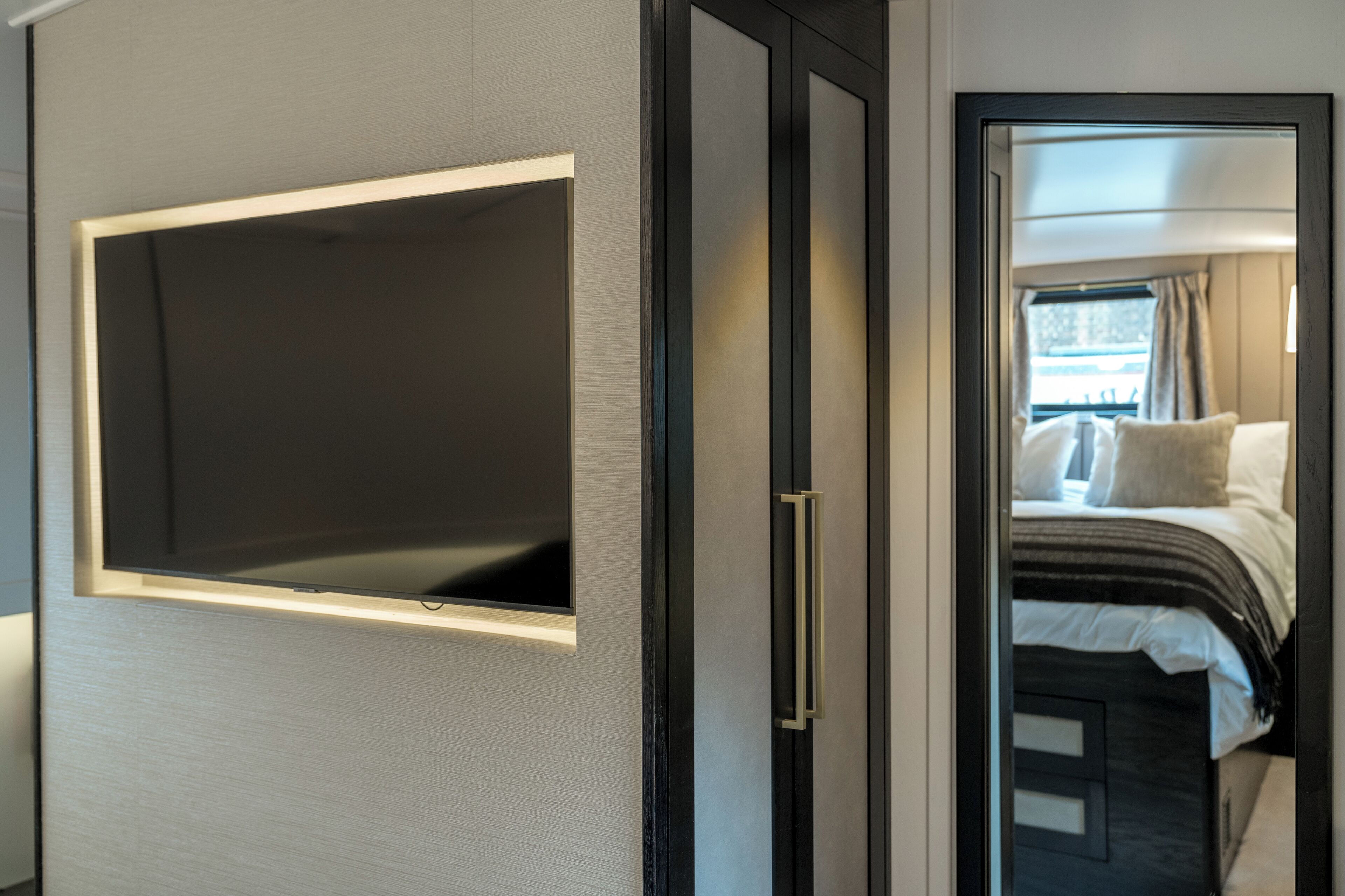 Une chambre d’hôtel moderne dotée d’un grand téléviseur à écran plat fixé au mur, d’un lit avec une tête de lit noire et d’une porte donnant sur un balcon agrémenté de rideaux.