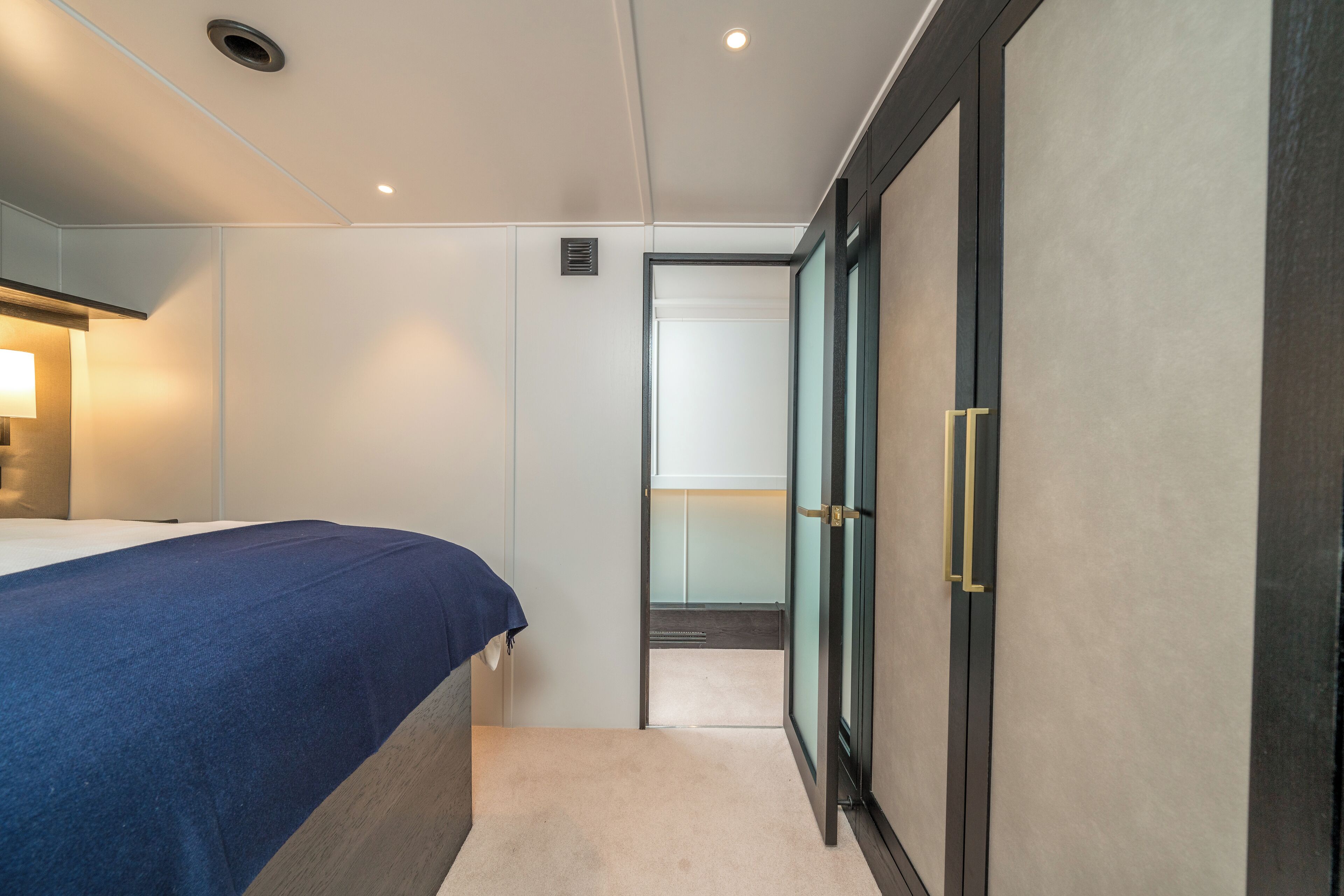 A hotel room with a bed, a bedside table with a lamp, a wardrobe, and a door leading to another room.