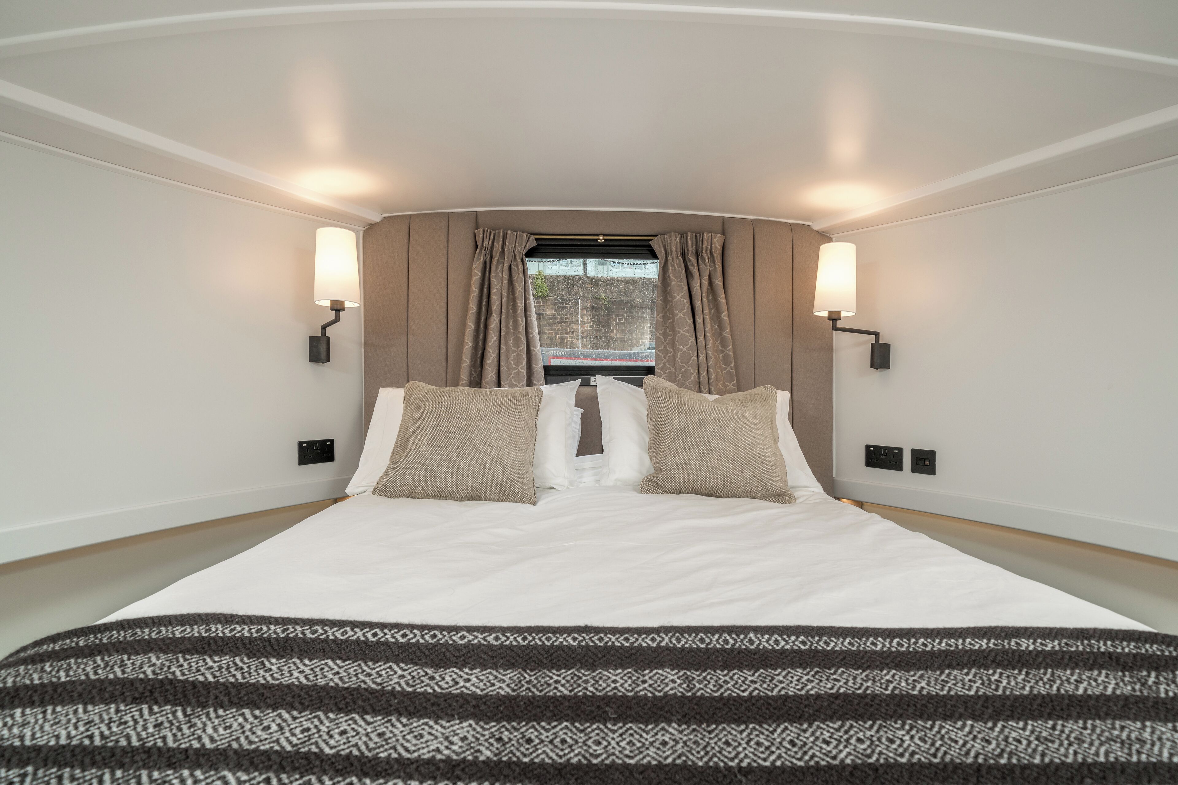 Une chambre d’hôtel moderne avec un grand lit, deux lampes fixées au mur et une fenêtre avec des rideaux.