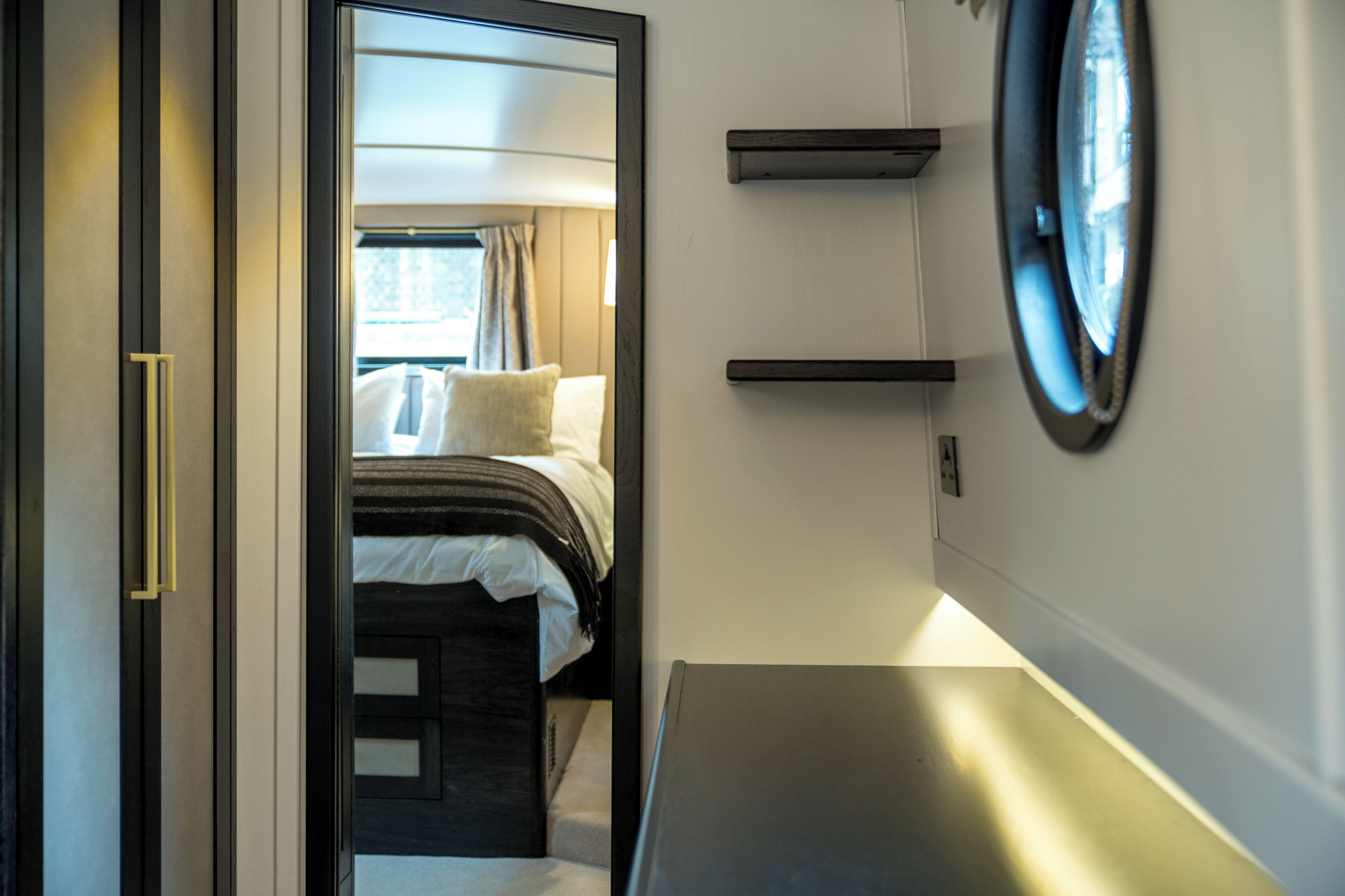 A narrow doorway leading into a bedroom with a bed, a bedside table, and a mirror on the wall.