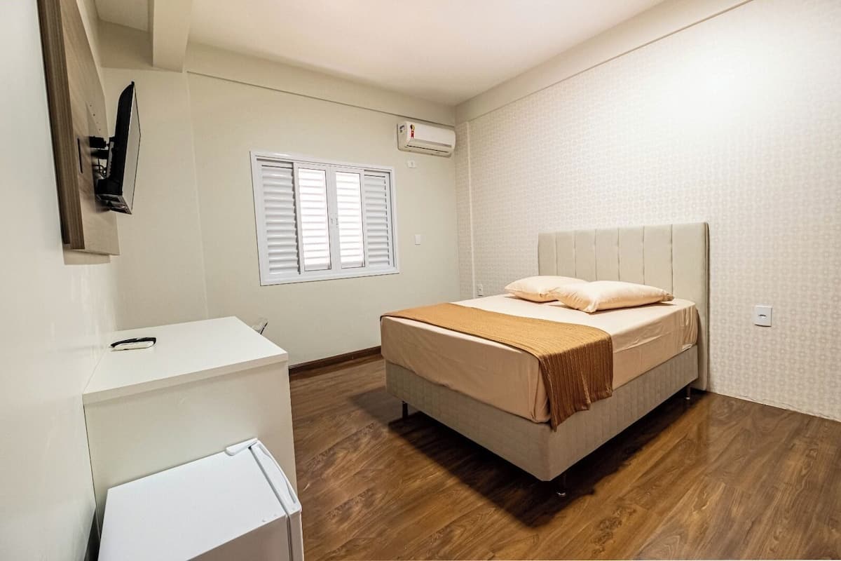 A bedroom with a bed, a desk, and a window with shutters.