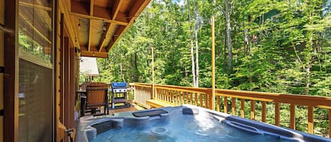 A hot tub on a wooden deck with a view of a forest.
