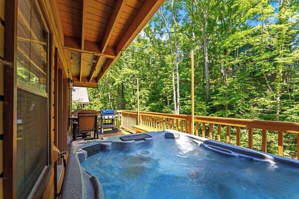 A hot tub on a wooden deck with a view of a forest.
