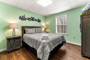 Une chambre à coucher comprenant un lit, deux lampes de chevet, une table de chevet, une fenêtre avec des stores et un élément décoratif fixé au mur.