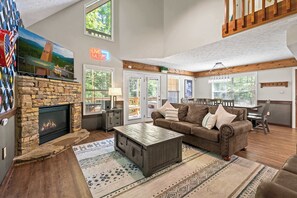 A spacious living room with a stone fireplace, a large flat-screen TV, a brown leather sofa, and a wooden coffee table.