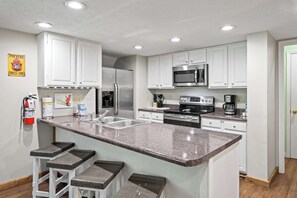 A kitchen with white cabinets, stainless steel appliances, a granite countertop, and bar stools.