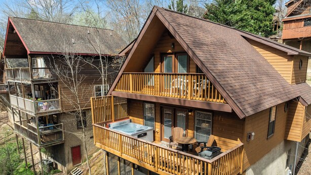 Een houten vakantiehuis met twee verdiepingen, een balkon, een hottub en uitzicht op het omliggende bos.