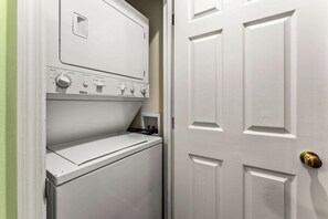 Une buanderie équipée d’un lave-linge et d’un sèche-linge à chargement frontal, d’une porte avec une poignée de porte en laiton et d’une petite étagère sur laquelle sont posés divers objets.