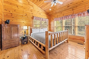 Quarto de cabana de madeira com cama, mesa de cabeceira, abajur e armário.