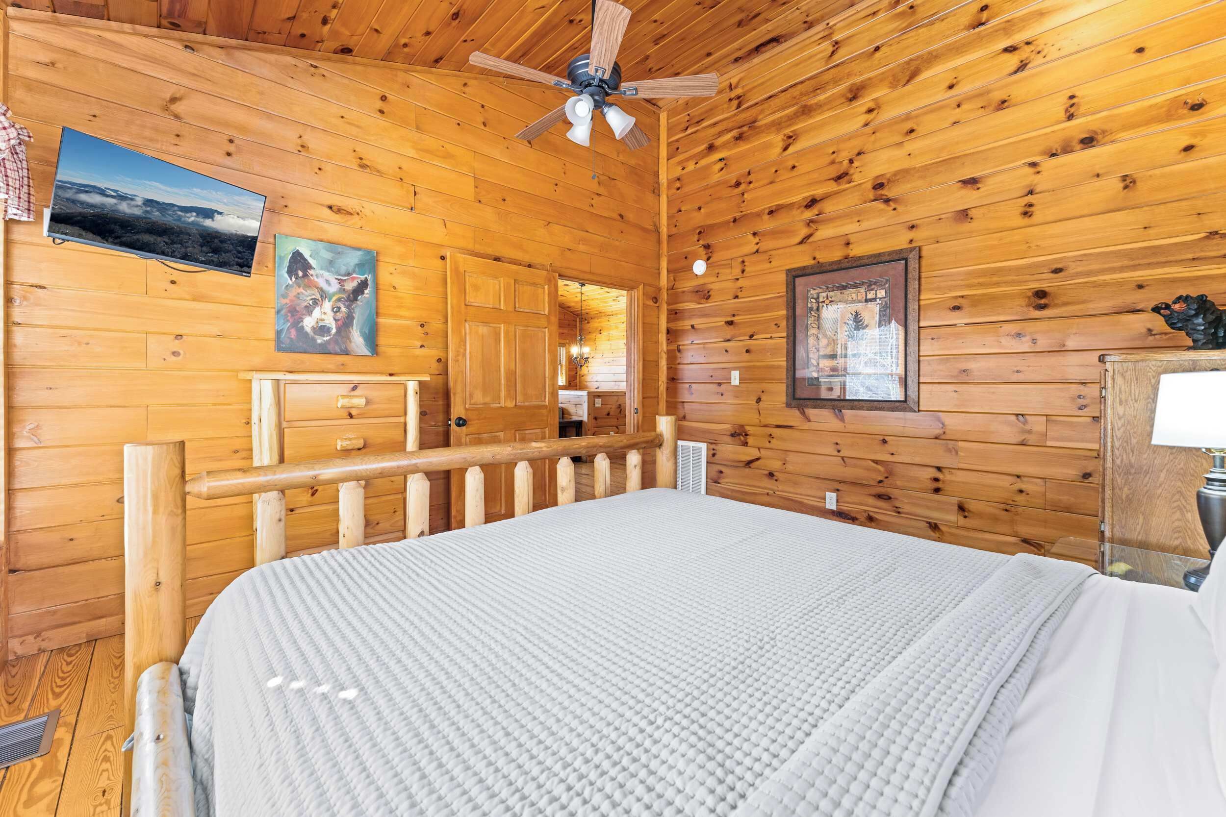 L’intérieur d’une cabane en bois comprend un lit, un ventilateur de plafond, des murs en bois et une porte donnant sur une autre pièce.