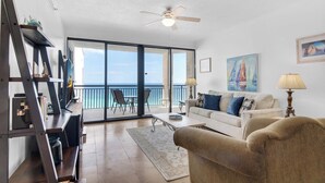 A spacious living room with a balcony, a ceiling fan, and a view of the ocean. - 🌴🌞🌴Beachfront Condo | Seasonally Heated Pool | Navarre Towers 1205🌴🌞🌴 (Navarre Beach)
