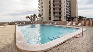 A swimming pool with lounge chairs and a tall building in the background. - 🌴🌞🌴Beachfront Condo | Seasonally Heated Pool | Navarre Towers 1205🌴🌞🌴 (Navarre Beach)