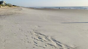 A wide, sandy beach with footprints leading towards the water.