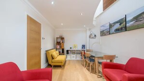 A compact living space with a dining area, two red sofas, a yellow armchair, and a bookshelf. - Great flat near St Pauls Cathedral (London)