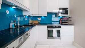 A compact kitchen with white cabinets, a black countertop, a built-in oven, and a microwave. - Great flat near St Pauls Cathedral (London)