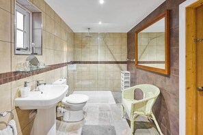 Clean bathroom with a white sink, toilet, and glass shower enclosure, featuring a wicker chair for seating.